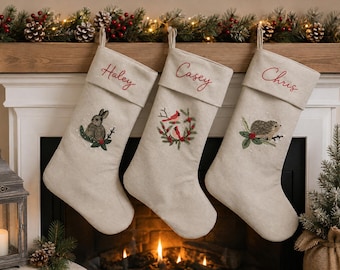 May include: Three beige fabric Christmas stockings with embroidered cuffs. The first features a rabbit, the second a wreath with two red birds, and the third a hedgehog. Each cuff is personalized with the names Haley, Casey, and Chris in red.