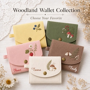 May include: Five fabric wallets from the Woodland Wallet Collection, each featuring a snap closure and embroidered nature motifs including berries, mushrooms, flowers, and moths. Some wallets are personalized with names like Anna, Emma, and Emily.