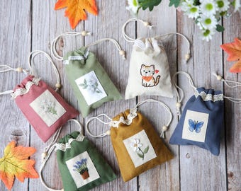 May include: A collection of small, colorful drawstring bags with embroidered floral and animal designs. The bags are in various colors, including pink, green, and blue, and are decorated with lace trim and wooden beads. The background is a wooden surface.