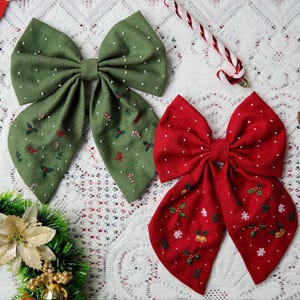 May include: Two large fabric bows, one green and one red, with white polka dots. The green bow has embroidered candy canes and holly. The red bow features embroidered snowflakes, bells, and holly. A festive holiday theme.