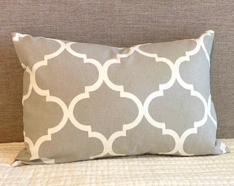 May include: A rectangular decorative pillow with a gray background and a white quatrefoil pattern. The pillow is resting on a white surface and against a gray headboard.