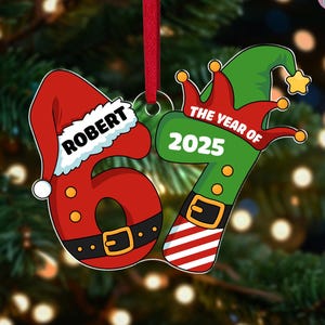 May include: A Christmas ornament shaped like the number 67, with a Santa hat on the 6 and an elf hat on the 7. The ornament is red and green, with the name "ROBERT" on the Santa hat and "THE YEAR OF 2025" on the elf hat.