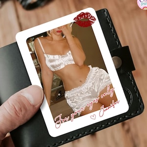 Puede incluir: Una tarjeta muestra un conjunto de lencería de satén blanco, con sujetador y shorts. La tarjeta tiene una marca de beso de lápiz labial rojo y el texto "For your eyes only Jennifer" en cursiva. La tarjeta se sostiene en una cartera de cuero negro.