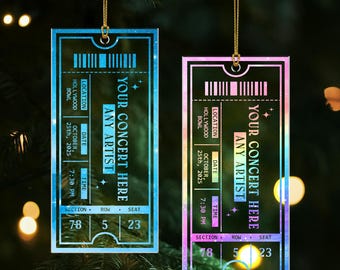 May include: Two rectangular concert ticket ornaments with gold hanging strings. The tickets are blue and pink with the text "YOUR CONCERT HERE ANY ARTIST" and details including the date, time, and location.
