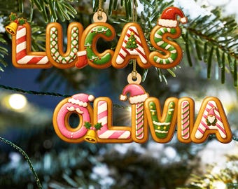 May include: Christmas tree ornaments spelling out the names "LUCAS" and "OLIVIA" in gingerbread cookie style. The letters are decorated with red, white, green, and pink icing, and festive holiday details like Santa hats and bells.