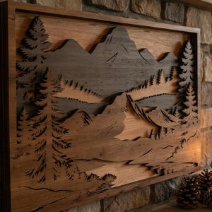 Peut inclure: Une œuvre d'art murale en bois représentant un paysage de montagnes et de forêts en couches. L'œuvre est encadrée dans un bois foncé et présente un fini veiné naturel. La conception comprend des découpes détaillées d'arbres et de montagnes.