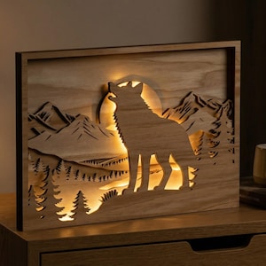 May include: Wooden light-up wall art depicting a howling wolf against a mountain and forest scene. The layered design creates a 3D effect, illuminated by warm light. A decorative piece for home interiors.