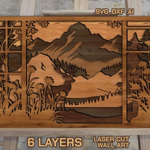 May include: Laser-cut wooden wall art depicting a mountain landscape with a deer, trees, and flowers. The artwork is made of six layers of wood and features the text "6 LAYERS" and "LASER CUT WALL ART".