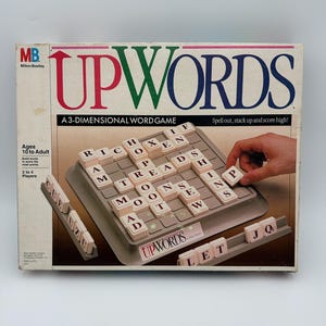 May include: A vintage Upwords board game box with the game board and tiles visible. The box features the game title in red, green, and blue. The game board has letter tiles in play, and the box reads "A 3-DIMENSIONAL WORD GAME".