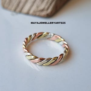 Puede incluir: Un anillo trenzado con tres colores metálicos: plata, oro y oro rosa. El anillo tiene un diseño de cuerda trenzada. El texto "MAYAJEWELLERYART925" es visible.