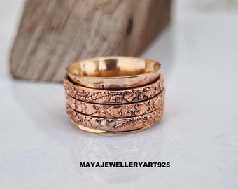 May include: A copper-colored ring with an intricate floral design. The ring has a spinning outer band and the text "MAYAJEWELLERYART925". The ring is displayed on a white surface with a wooden block in the background.