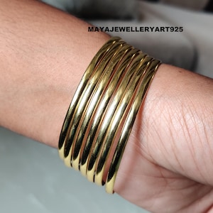 May include: A set of seven gold-colored bangles stacked on a wrist. The bangles are smooth and shiny, reflecting light. The text "MAYAJEWELLERYART925" is visible in the upper right corner.