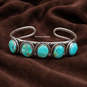May include: A silver cuff bracelet featuring five oval turquoise stones with brown matrix patterns. Each stone is set in a twisted rope border on a textured silver band. The text MAYAJEWELLERYART925 is visible on the inner surface of the bracelet.