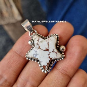May include: A star-shaped pendant with a white and brown stone centre, set in a silver frame. The pendant has a textured border and a bail for a chain. The text "MAYAJEWELLERYART925" is visible.