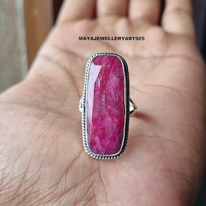 May include: A rectangular silver ring featuring a large, vibrant pink gemstone. The gemstone is set within a textured silver frame. The ring is displayed on a hand, with the text "MAYAJEWELLERYART925" visible.