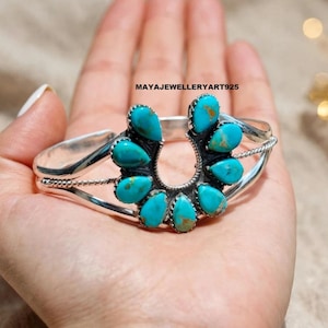 May include: A silver cuff bracelet featuring a horseshoe-shaped centrepiece adorned with eight teardrop-shaped turquoise stones. The metal band has a twisted rope texture along the sides. The text MAYAJEWELLERYART925 is visible above the bracelet.