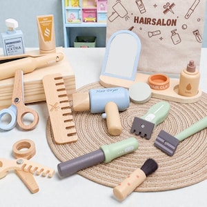 Pode incluir: Um conjunto de brinquedos de madeira para salão de cabeleireiro com várias ferramentas, incluindo um secador de cabelo, tesoura, pente, espelho e frascos. O conjunto apresenta cores pastel e o texto "HAIRSALON" numa bolsa de lona. Os brinquedos estão dispostos sobre uma esteira tecida.