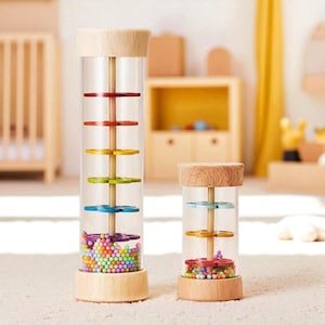 May include: Two wooden and clear plastic rainmakers. The larger one has red, orange, yellow, green, and blue discs. The smaller one has orange, yellow, and red discs. Both have colorful beads at the bottom and wooden tops.
