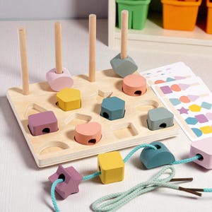 Pode incluir: Brinquedo de classificação de formas de madeira com uma base de madeira clara e formas geométricas coloridas. Inclui pinos, blocos e uma corrente de formas. As formas são em várias cores, incluindo rosa, amarelo, azul e roxo. Um brinquedo educativo divertido para crianças.