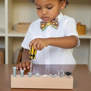 Może przedstawiać: Dziecko w wzorzystej muszce i białej koszuli używa żółto-czarnego śrubokręta na drewnianej desce z różnymi metalowymi elementami mocującymi. Deska stoi na brązowym stole.