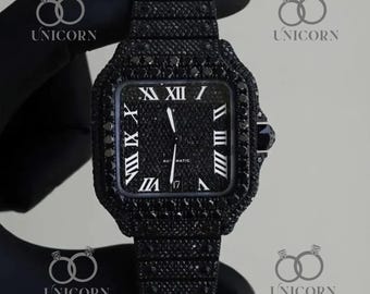 May include: A black wristwatch with a square face and a matching black band. The watch face features white Roman numerals and hands, with the word "AUTOMATIC" and the number "17" visible. The watch is encrusted with black stones.