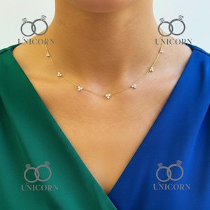 Puede incluir: Un delicado collar de oro con pequeñas gemas brillantes dispuestas en un patrón floral. El collar lo lleva una persona con una blusa verde y azul. Una fina pieza de joyería.