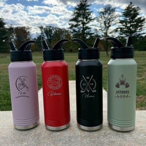 May include: Four insulated water bottles in pink, red, black, and sage green. Each bottle has a black lid and a silver base. The bottles are engraved with personalized designs, including a baseball, swimming logo, golf club, and weightlifting figure.