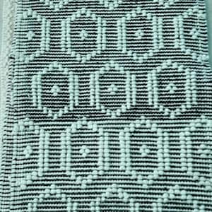 May include: Close-up of a black and white patterned rug. The rug features a repeating geometric design with horizontal stripes and dotted accents. The color scheme is neutral, making it suitable for various interior styles.