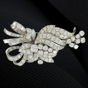 May include: A vintage brooch with a floral and bow design, set with numerous sparkling diamonds. The brooch is crafted from silver-toned metal. The design incorporates a central large diamond and baguette-cut diamonds, creating a luxurious look.