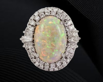 Puede incluir: Anillo de ópalo ovalado con un halo de pequeños diamantes y detalles de diamantes. El ópalo tiene un juego de colores con destellos verdes, amarillos y naranjas. El anillo está engastado en plata u oro blanco.
