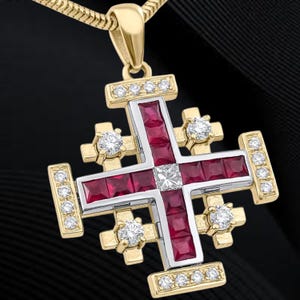 May include: A gold-tone pendant necklace featuring a Jerusalem cross design. The cross has a red center with square-cut stones, accented with clear gemstones and a central square stone. The necklace chain is also gold-toned.