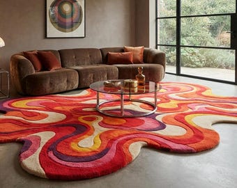 May include: An irregular, organic-shaped area rug featuring a vibrant, multi-layered pattern of wavy, flowing lines in shades of red, orange, yellow, pink, and deep purple, with a textured, tufted surface that covers a large portion of the floor.