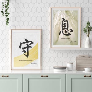 Könnte beinhalten: Zwei gerahmte Kunstdrucke mit japanischer Kalligraphie. Einer zeigt ein schwarzes Symbol über einem gelben Pinselstrich mit dem Text "Shu, Not Closed, Just Protected". Der andere zeigt ein schwarzes Symbol mit dem Text "Iki, A Place to Breathe."
