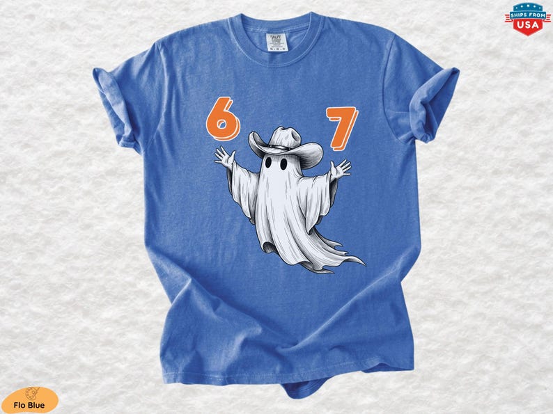 May include: A blue short-sleeved t-shirt featuring a graphic of a white ghost wearing a cowboy hat with its arms outstretched. The numbers 6 and 7 are printed in orange above the ghost. The shirt has a crew neckline and a casual, relaxed fit.