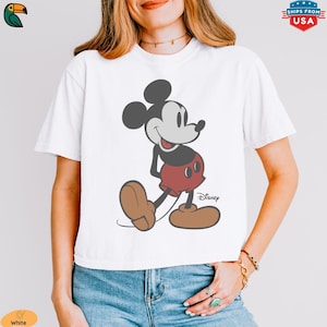 K&ouml;nnte beinhalten: Wei&szlig;es T-Shirt mit einer klassischen Mickey Mouse-Illustration. Die Zeichentrickfigur ist in Schwarz, Rot und Braun dargestellt. Das Disney-Logo befindet sich unten rechts. Ein l&auml;ssiges Oberteil f&uuml;r Disney-Fans.