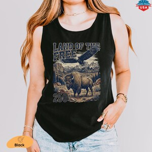 May include: Black tank top featuring a graphic with the text "LAND OF THE FREE" above an eagle and a bison in a mountain landscape. The number "250" is below the bison. The tank top is sleeveless.