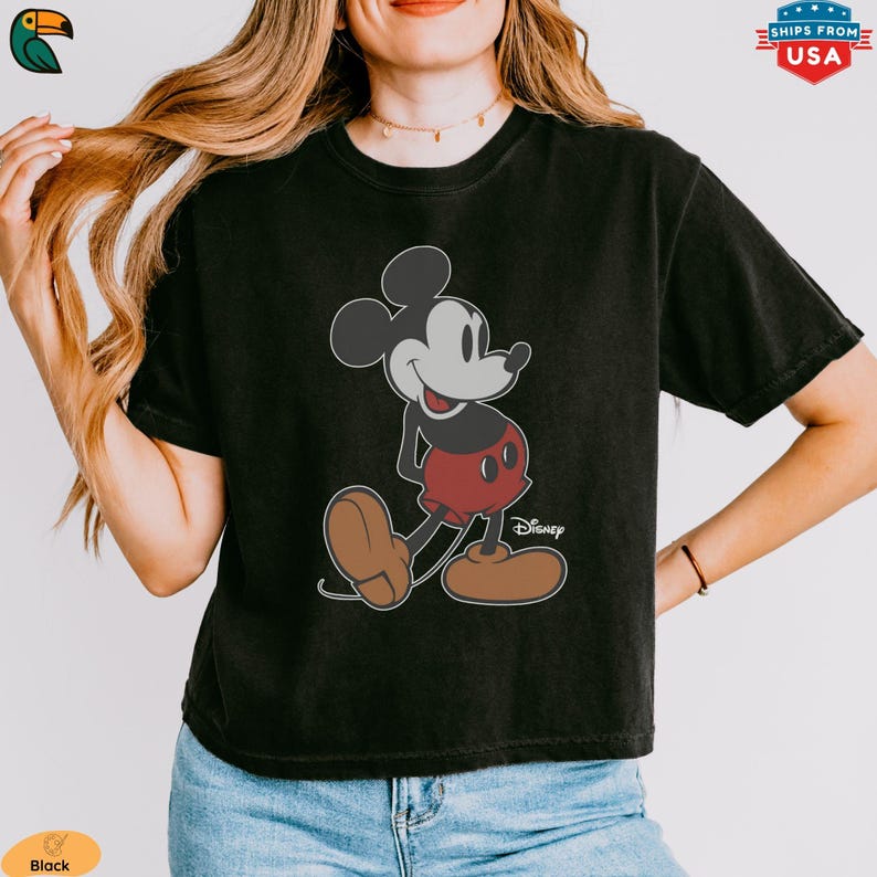 K&ouml;nnte beinhalten: Schwarzes T-Shirt mit einer Mickey Mouse-Grafik. Die Zeichentrickfigur ist in Schwarz, Rot und Braun gehalten. Das Disney-Logo ist unter der Figur aufgedruckt. Das T-Shirt ist ein Freizeitartikel. Das Bild zeigt ein klassisches Disney-Design.