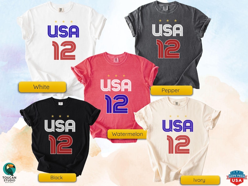K&ouml;nnte beinhalten: F&uuml;nf T-Shirts in verschiedenen Farben: Wei&szlig;, Pfeffer, Wassermelone, Schwarz und Elfenbein. Jedes Shirt zeigt den Text "USA 12" in einer kr&auml;ftigen, stilisierten Schrift mit drei Sternen &uuml;ber "USA".
