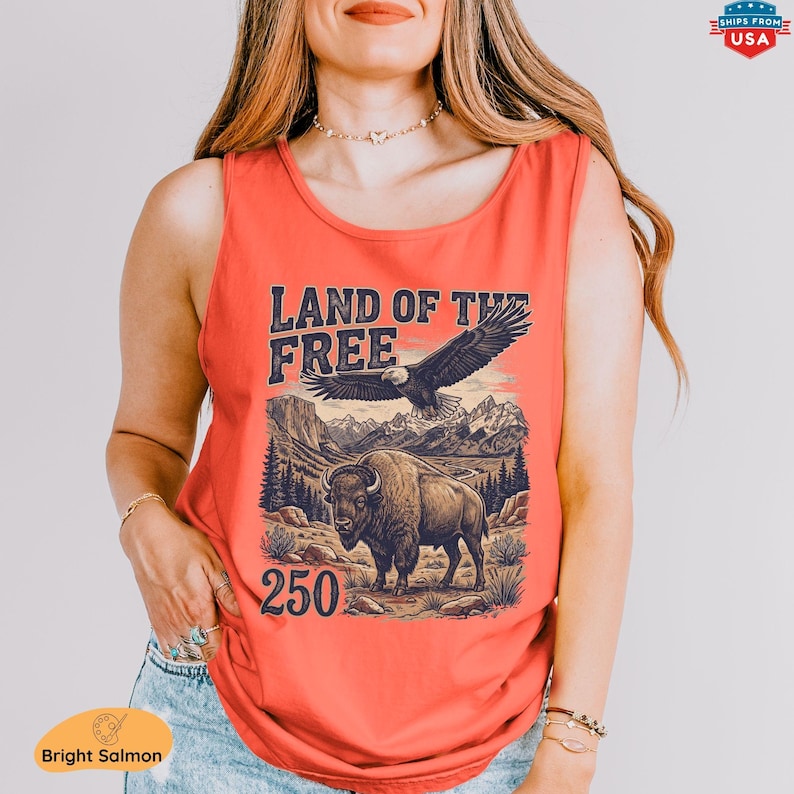 May include: Bright salmon tank top with a graphic featuring an eagle, bison, and mountain landscape. The text "LAND OF THE FREE" and the number "250" are printed on the front. The tank top is sleeveless.
