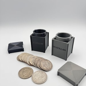 May include: A collection of silver coins and two coin holders, one black and one gray, with the text "US DOLLAR" on the side. Two gray square lids are also present. The coins are arranged in a row.