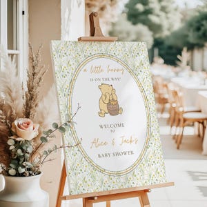 May include: A baby shower welcome sign on an easel. The sign features a Winnie the Pooh illustration with the text "a little bunny is on the way!" and "Welcome to Alice & Jack's Baby Shower."