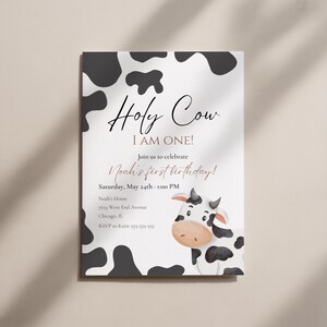 May include: A white invitation card featuring a black and white cow pattern and a cartoon cow illustration. The text reads "Holy Cow I AM ONE!" and invites guests to a first birthday party. Includes date, time, and location details.