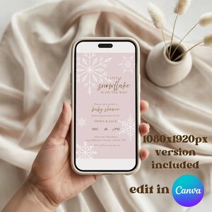K&ouml;nnte beinhalten: Ein Smartphone zeigt eine digitale Babyparty-Einladung auf hellrosa Hintergrund mit wei&szlig;en Schneeflocken-Illustrationen. Der Text lautet: A LITTLE snowflake IS ON THE WAY! Please join us for a baby shower honoring parents-to-be EMMA & JACK.