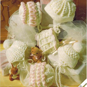 May include: A collection of handmade crochet baby hats and bonnets in cream and pink. The hats have pom-poms and ties. A small teddy bear and a bunny are also in the image. The text "PREMATURE CROCHET" is visible.