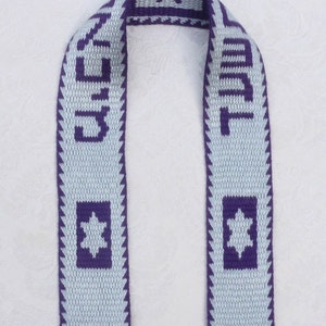 May include: A light blue and purple woven scarf with the word "Jerusalem" written in Hebrew on one side and the word "Jerusalem" written in English on the other side. The scarf also features a six-pointed star.