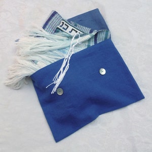 May include: A blue fabric pouch with two buttons and a white fringe. The pouch is open and a patterned prayer shawl with Hebrew writing is inside.