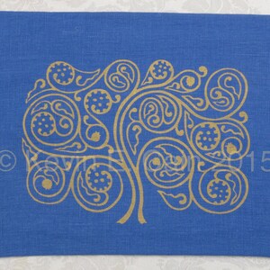 May include: A blue linen fabric with a gold-colored design of a stylized tree with intricate swirls and leaves. The design is reminiscent of Celtic knotwork.