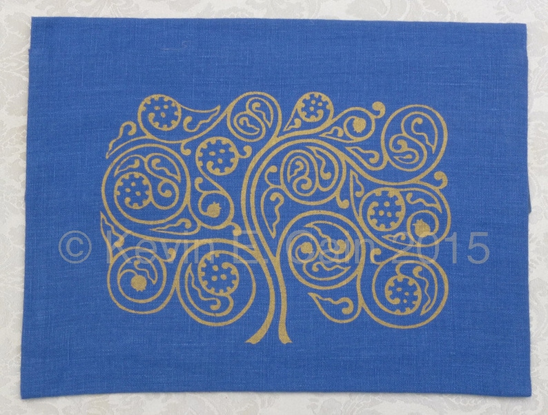 May include: A blue linen fabric with a gold-colored design of a stylized tree with intricate swirls and leaves. The design is reminiscent of Celtic knotwork.