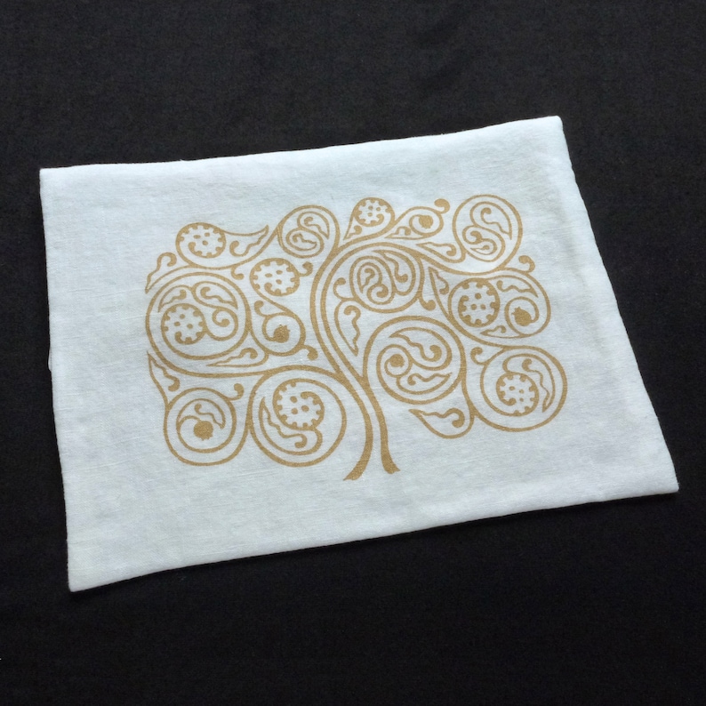 May include: White cotton tea towel with a gold paisley design printed on it. The design is a stylized tree with branches and leaves.