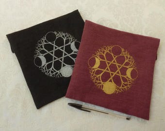 May include: Two fabric pouches with a moon and tree design. One pouch is black with a silver design and the other is burgundy with a gold design.